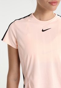 Ljusrosa Nike sport-t-shirt med korta ärmar. Har svarta detaljer på axlarna och ett luftigt texturerat mönster på tyget.