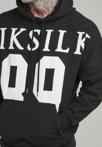 Felpa nera con stampa grafica bianca con la scritta "IKSILK" e il numero "90", realizzata in materiale morbido, con tasca frontale e cappuccio con coulisse.