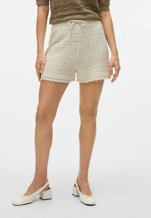 Femme portant un short en crochet couleur crème noué à la taille avec un nœud, associé à des chaussures slingback crème à petit talon bloc.