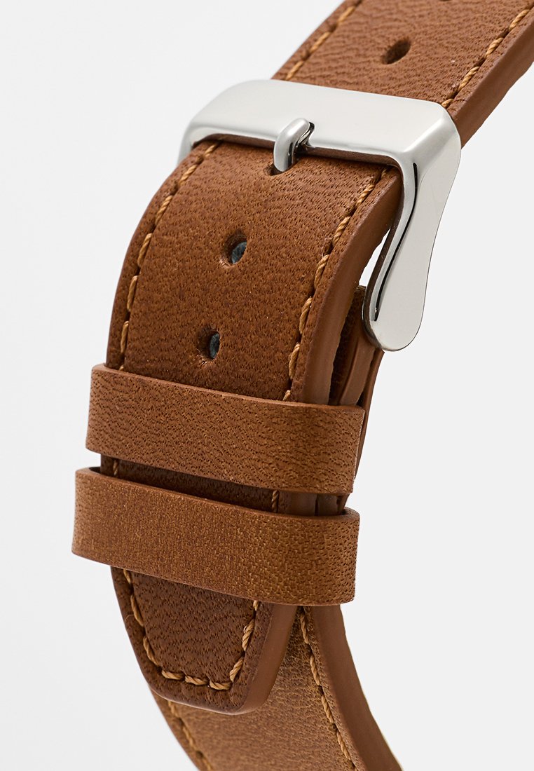 Correa de reloj de cuero marrón con textura lisa, hebilla de metal plateada y dos presillas. Cuenta con agujeros perforados para ajuste regulable.