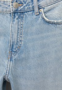 Ljust blå denimjeans med en strukturerad väv, kontrasterande orange sömmar och en metallknapp i midjan med en enkel femficksdesign.