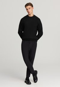 Czarny dzianinowy sweter z okrągłym dekoltem, w połączeniu z czarnymi zwężającymi się spodniami i błyszczącymi czarnymi butami, tworząc monochromatyczny zestaw.