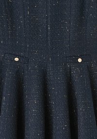Tissu en tweed bleu marine avec une finition texturée, arborant de petits boutons en argent sur les poches et des fils métalliques subtils tout au long.