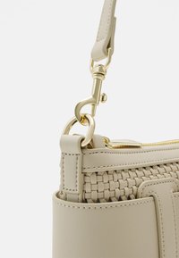 Beżowa torebka o plecionej fakturze, ze złotymi elementami i odpinanym paskiem. Posiada zamek błyskawiczny na górze oraz przeszycia po bokach.