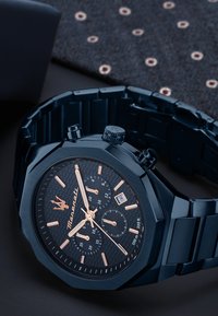 Schwarz octagonaler Uhr mit strukturiertem Zifferblatt, roségoldenen Akzenten, Chronographen-Unterzifferblättern und passendem Armband. Wasserdicht bis 100 Meter.