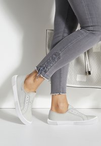 Graue Leinenschlupfschuhe mit weißer Gummisohle, die zwei Reihen von Ösen und eine strukturierte Oberfläche aufweisen. Getragen mit grauen, zerschlissenen Skinny Jeans.