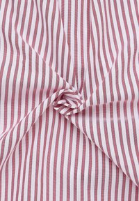 Tessuto di cotone rosa chiaro con sottili righe verticali rosse e grigie, caratterizzato da una texture morbida e una leggera lucentezza, raccolto al centro.