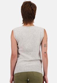 Hellgrauer ärmelloser Pullover mit strukturierter Oberfläche, mit Rundhalsausschnitt und leicht lockerer Passform, getragen zu olivgrünen Hosen.