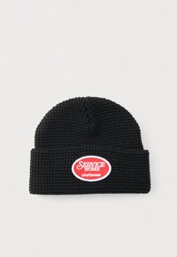 Μαύρο πλεκτό σκουφάκι με υφή μοτίβου. Διαθέτει κόκκινη και λευκή οβάλ ετικέτα με το κείμενο «SERVICE WORKS chefswear». Σχέδιο με διπλωμένη υπόδη.