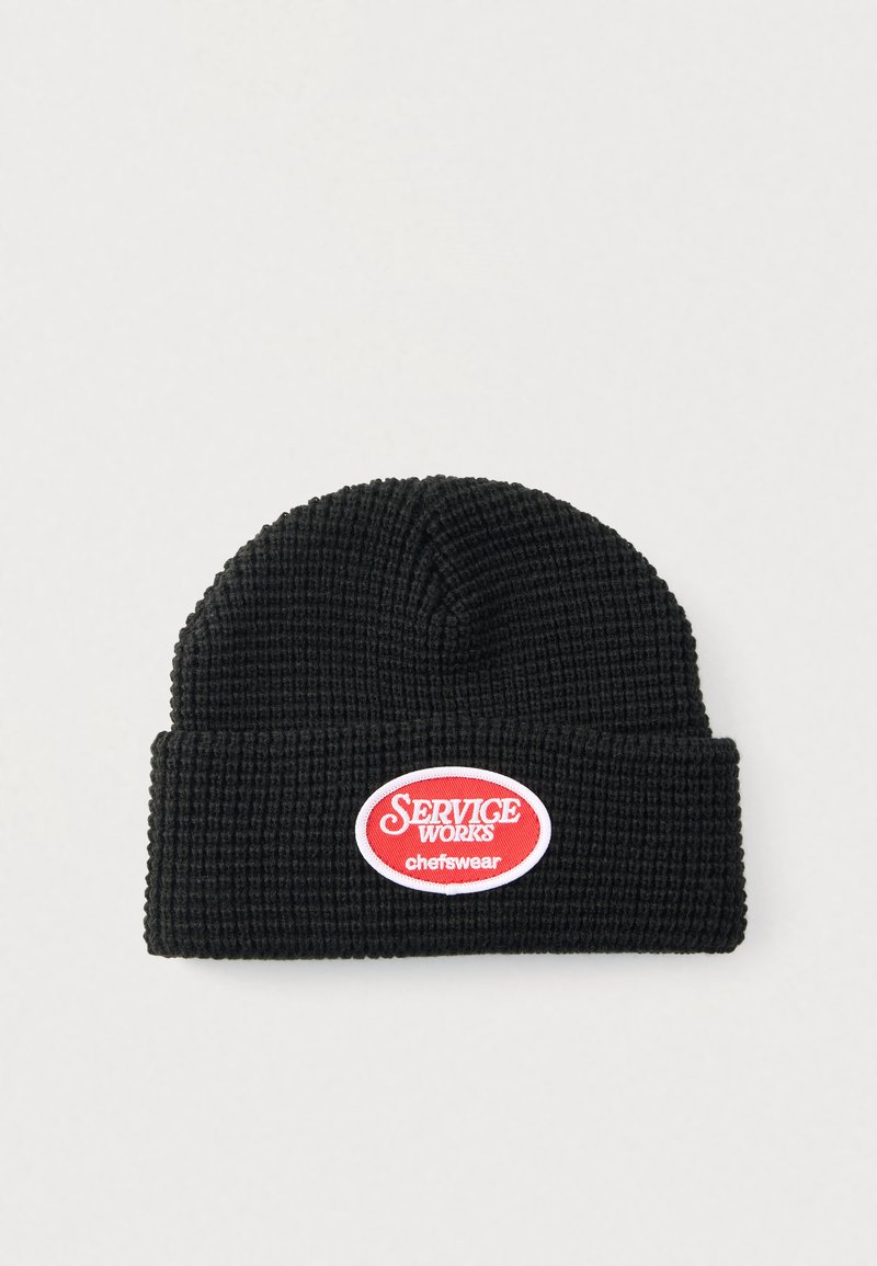 Μαύρο πλεκτό σκουφάκι με υφή μοτίβου. Διαθέτει κόκκινη και λευκή οβάλ ετικέτα με το κείμενο «SERVICE WORKS chefswear». Σχέδιο με διπλωμένη υπόδη.