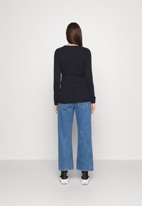 Granatowy sweter w prążki z długimi rękawami, zestawiony z jasnoniebieskimi dżinsami typu wide-leg. Czarnskie skarpetki i białe sneakersy dopełniają strój.