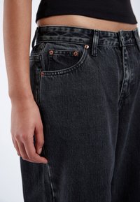 High-waisted black denim jeans with a slight acid wash, featuring copper rivets and a smooth, sturdy texture. Front pocket visible.