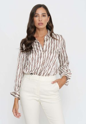 Camicia bianca con motivo a catena marrone, abbottonata sul davanti e maniche arrotolate, abbinata a pantaloni bianchi a vita alta. Tessuto dalla superficie liscia.