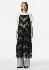 Melns mežģīņu daudzslāņu kleita ar smalkām ziedu rakstiem, nēsāta pār baltu T-kreklu. Aprīkota ar plānām siksniņām un ceļgalu garuma dizainu pār pelēnām džinsu biksēm.