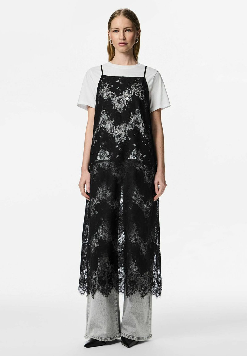 Melns mežģīņu daudzslāņu kleita ar smalkām ziedu rakstiem, nēsāta pār baltu T-kreklu. Aprīkota ar plānām siksniņām un ceļgalu garuma dizainu pār pelēnām džinsu biksēm.