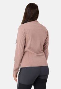 Jasnoróżowa polarowa kurtka z podwyższonym kołnierzem, długimi rękawami i dopasowanym krojem. Gładka tekstura, minimalne szwy i brak widocznego okuć.