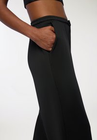 Czarne spodnie sportowe o gładkiej fakturze, z elastycznym pasem i bocznymi kieszeniami, charakteryzujące się tapered designem i minimalnymi detalami szwów.