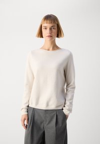 Cream-colored, long-sleeve sweater with a round neckline and soft texture, paired with gray pleated trousers. Simple and minimalistic design.