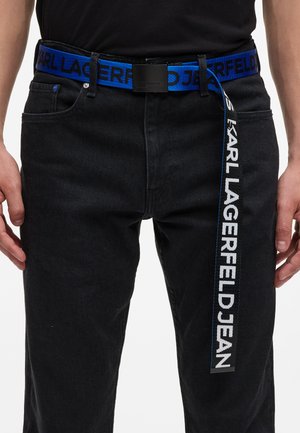 Ceinture en coton bleu avec inscription noire "KARL LAGERFELD JEAN." Boucle en métal. Portée sur un pantalon en denim noir.