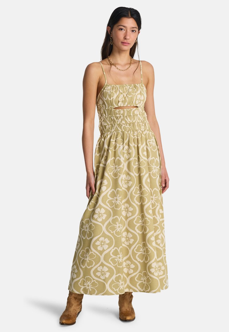 Μακρύ φόρεμα σε ανοιχτό πράσινο με λευκό λουλουδάτο σχέδιο, με κουρασμένο μπούστο και ρυθμιζόμενους ιμάντες. Φορεμένο με ταμπά μποτάκια αστραγάλου.