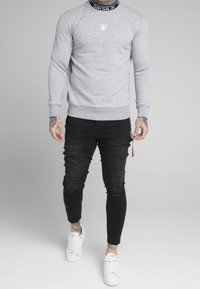 Grå sweatshirt med ribbad krage, med en liten vit logotyp. Matchad med svarta slitna slim-fit jeans och vita sneakers.