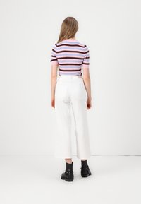 Pruhovaný svetr s krátkým rukávem v růžové, modré a hnědé barvě doplněný bílými kalhotami s širokými nohavicemi. Outfit doplňují černé kotníčkové boty.