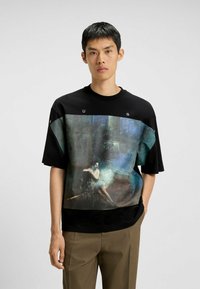 Camiseta negra de gran tamaño y manga corta con una impresión de obra de arte texturizada en colores suaves en la parte frontal. Los acentos incluyen letras en negrita en el hombro.