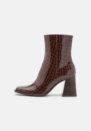 Bottine en faux cuir brun avec une texture crocodile, bout carré et un talon en bois épais. Fini lisse, silhouette épurée.