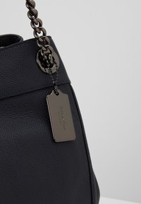 Gros plan sur un sac à main en cuir noir texturé avec une large chaîne métallique en bandoulière et une étiquette gravée Coach New York.
