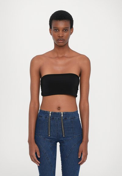 Crop top noir sans bretelles associé à un jean en denim bleu taille haute avec des zippers avant et des coutures angulaires. Texture de tissu lisse.
