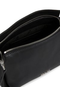 Borsa nera in pelle con texture liscia, dotata di una cerniera argentata e fodera. Design minimalista con un logo impresso su un lato.