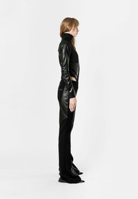 Top de cuello alto de cuero negro combinado con pantalones negros de tiro alto que presentan detalles de cuero, diseño ajustado y una silueta estilizada.
