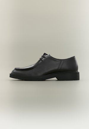 Scarpa da uomo elegante in pelle nera con lacci, suola spessa in gomma, design moc toe e tacco basso vista laterale su sfondo neutro.