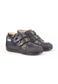 Zapatos de cuero negros con punteras de goma texturizada, que cuentan con dos correas de Velcro y acentos brillantes. El diseño incluye un emblema púrpura.