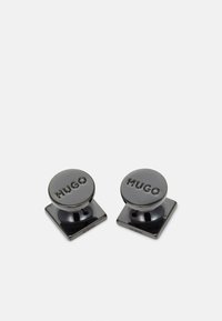 Gemelli rotondi neri con una finitura lucida e il logo "HUGO" inciso, montati su una base quadrata. Il materiale sembra metallico.
