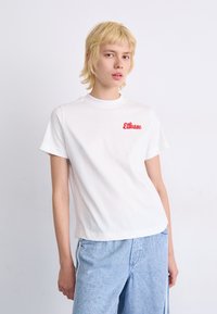 Hvit bomull t-skjorte med korte ermer, med en rød brodert "Ellesse"-logo på venstre bryst og en avslappet passform.