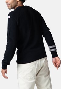Maglione nero a maglia con colletto a girocollo a coste, dotato di strisce grigie di accento sulle maniche e di una piccola toppa con logo vicino alla spalla.