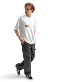 Witte T-shirt met een kleurrijk grafisch ontwerp aan de voorkant, gecombineerd met donkergrijze cargo-broek met meerdere zakken en een relaxte pasvorm.