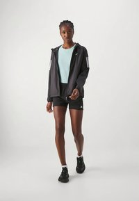 Zwarte lichte jas met witte strepen, aquakleurig T-shirt en zwarte shorts. Draag met zwarte sportschoenen met groene accenten.