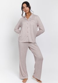 Conjunto de ropa de casa que incluye una camiseta de manga larga texturizada en rosa claro con botones y pantalones anchos a juego con un sutil patrón y detalles en blanco.