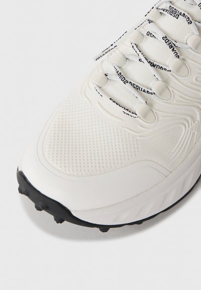 White athletic shoe front with textured fabric upper, black tread sole, and white laces featuring black printed text.