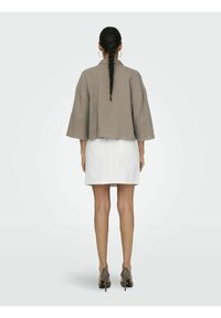 Khaki cropped jacket with wide sleeves, textured fabric, and a boxy fit, paired with a white denim skirt and taupe high-heeled shoes.