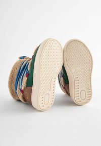 Bottes beige duveteuses avec des accents verts et bruns, dotées de lacets bleus et d'une semelle en caoutchouc à motif pour une adhérence optimale.