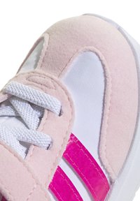 Deportivas rosas y blancas con parte superior de suave ante, paneles de malla y rayas rosas brillantes. Cuenta con cordones planos blancos y un cuello acolchado.