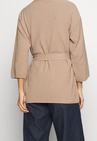Beige, textuur gebreide cardigan met een strik op de rug, driekwart mouwen en een relaxte pasvorm. Heeft een rechte zoomlijn en minimale details.