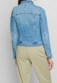 Light blue denim jacket with a fitted silhouette, classic collar, and buttoned cuffs. Features stitched detailing and a smooth texture.