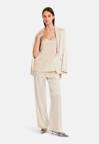 Ivory Satin-Camisole in Kombination mit einem ivory Blazer und weiten Hosen, die eine glatte Textur und ein schlankes, modernes Design aufweisen. Silberne Absätze runden den Look ab.