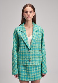 Set di giacca tweed e mini gonna in un motivo a quadri turchese e verde. Presenta grandi bottoni e un classico design con colletto a punta.