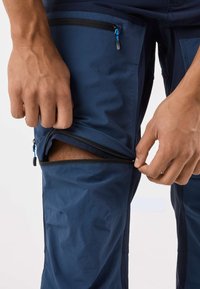 Marinblå zip-off-byxor med ett mjukt, lätt tyg. Synlig dragkedja på låret för att justera längden. Flera fickor ingår.