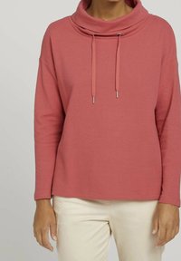 Bluza z mieszaniny bawełny z golfem w stonowanym różowym kolorze, z troczkami, fakturowaną powierzchnią i długimi rękawami, zestawiona z jasnobeżowymi spodniami.